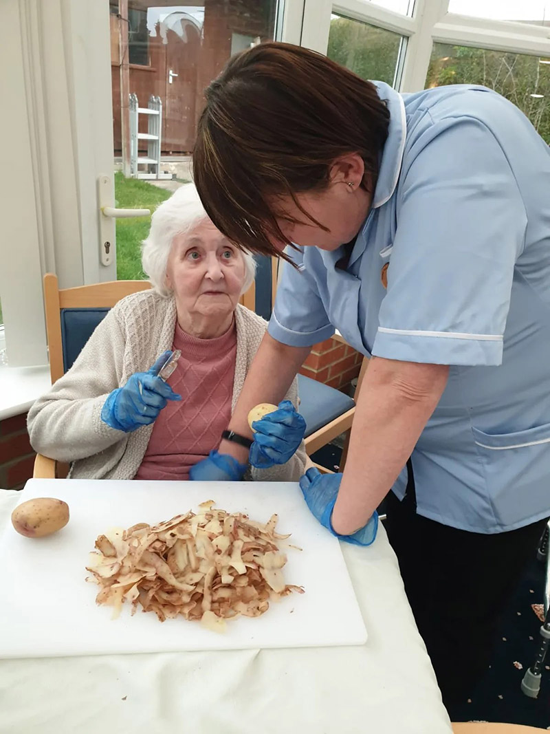Nursing home staff helping elderly woman peel potatoes