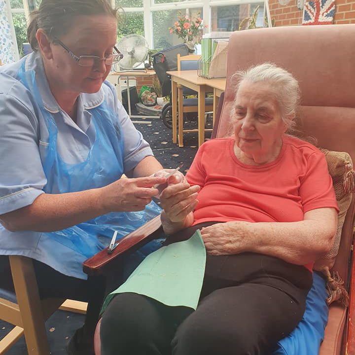 Nursing home staff taking care of an elderly woman's nails