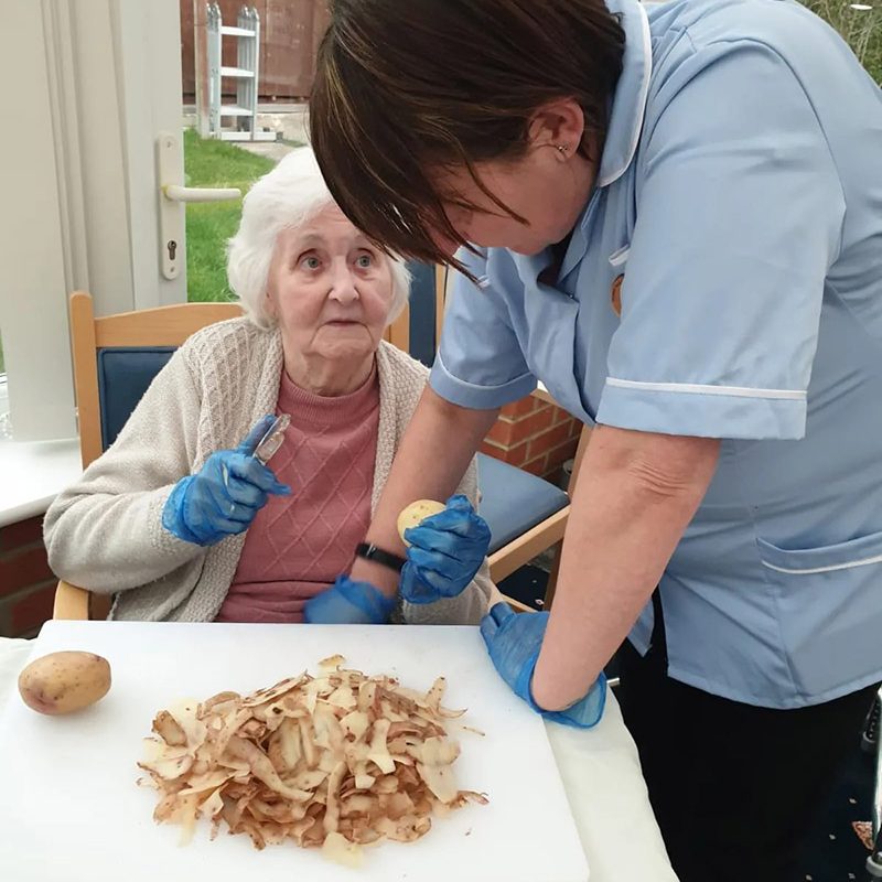 Nursing home staff helping elderly woman peel potatoes